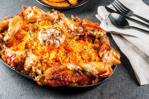 West African national cuisine. Jollof rice with grilled chicken wings and fried bananas plantains on gray stone table. 