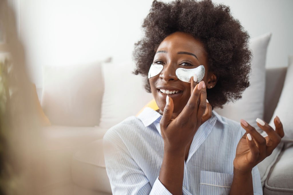 A-black-woman-applying-eye-cream-while-looking-at-the-mirror