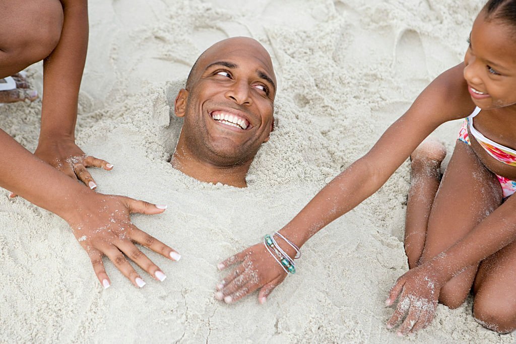 Family burying father in beach sand