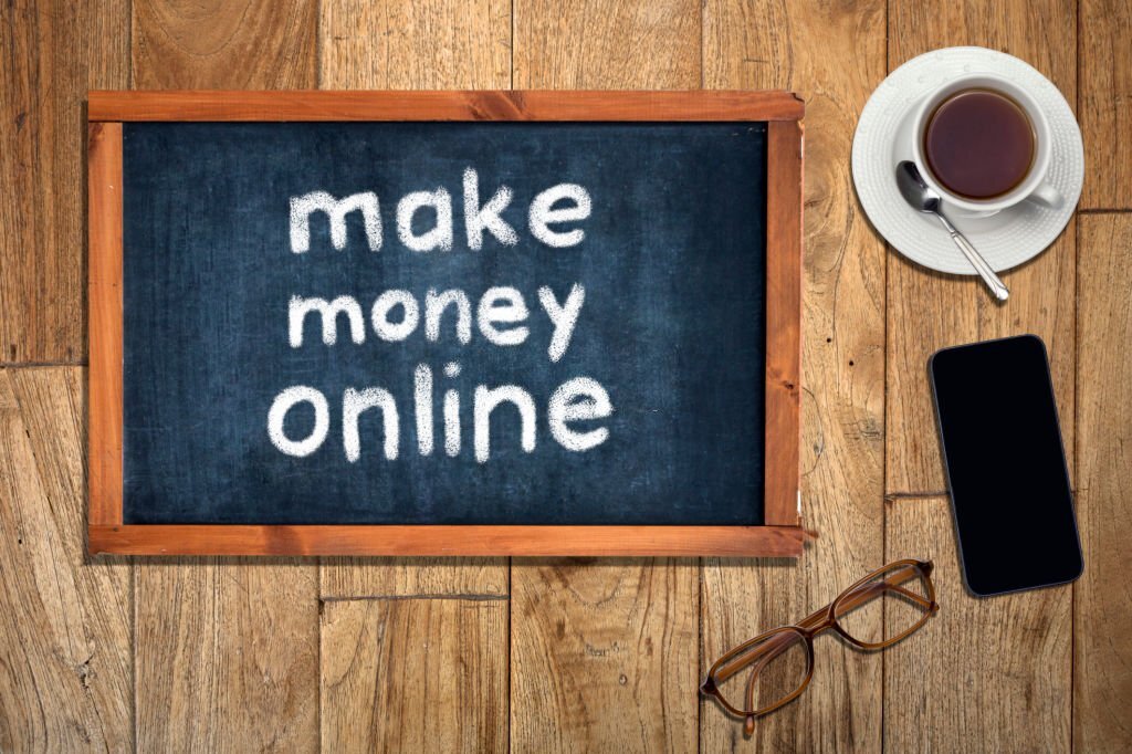 An image showing a table on which a cup of coffee, a phone, an eye glass, and a black board with the inscription "make money online"