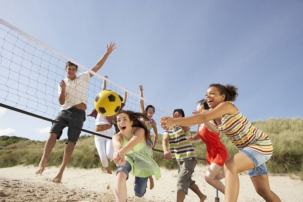 Two teams Of teenage friends having fun, playing volleyball on the beach together. 