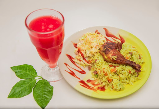 Nigerian Fried Rice with chicken laps and a cocktail drink.
