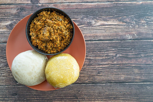 A Big plate containing a bowl of Egusi soup, one wrap of Garri and Pounded yam