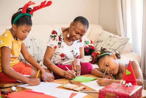 Smiling grandmother and her two granddaughters making Christmas cards together at home during the holidays