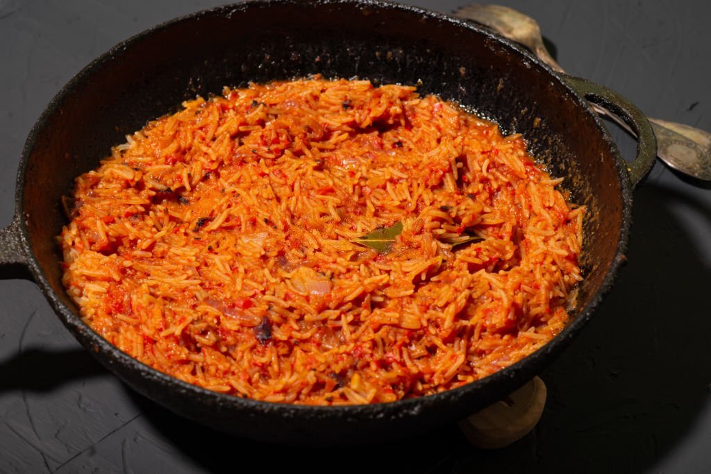 Jollof rice in a frying pan on a dark background. A traditional Nigerian dish of rice, tomatoes and spices.